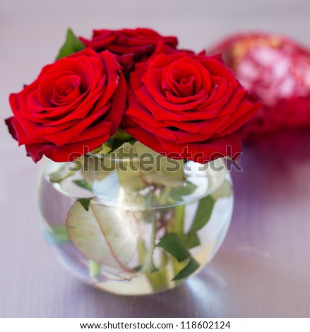 Round transparent vase with red roses on the table close-up