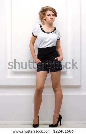 Beautiful young woman posing in black shorts, black heels and a military shirt and cap on a white background.