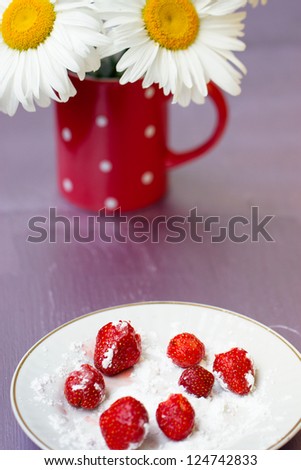 Strawberries in powdered sugar, next to a bouquet of daisies