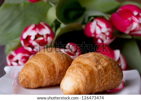Two croissants on a plate next to a bouquet of tulips