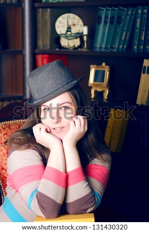 Fat girl in a striped sweater and hat on the background of the bookcase