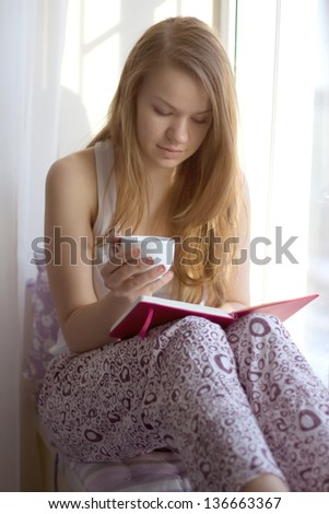 Young girl on the window sill in my pajamas with a cup of reading a book