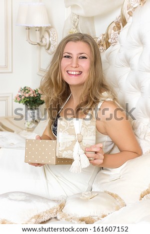 Stylish blond woman in black dress  in hotel apartment. Sexy girl gifts relaxing on bed at home luxury interior
