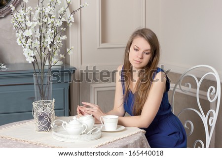Smiling beautiful girl in  dress sits at table in cosy cafe.