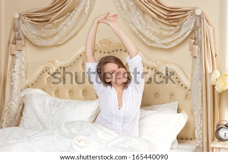 Tired sleepy woman waking up and yawning with a stretch while sitting in bed