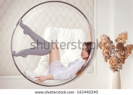 Girl in white tunic sitting in a chair suspended round