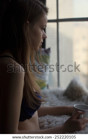 Woman in the morning. woman with neat body is holding a cup with hot tea or coffee and looking at the sunrise standing near the window in her home and having a perfect cozy morning