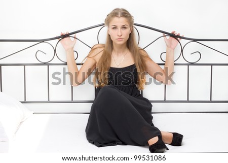 Beautiful girl in a dress and shoes on high heels sitting on a bed studio photography