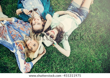 Trendy Hipster Girls Relaxing on the Grass . Summer lifestyle portrait of three hipster women laying on the grass enjoy nice day, wearing bright sunglasses. Best friends girls having fun, joy.