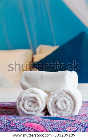 White bath towel rolled up on a bed in hotel room. Welcome guests.