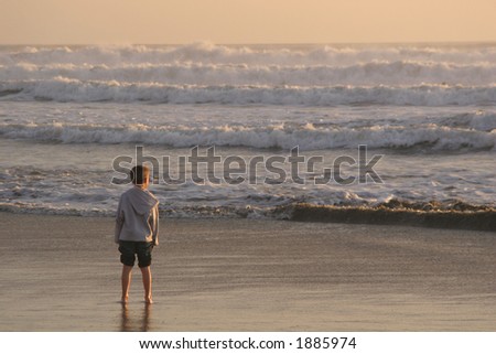A young boy on the beach in the evening light waiting for the next wave to come in.