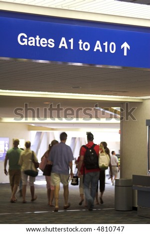 Airport gate sign and travelers heading to the boarding gates.