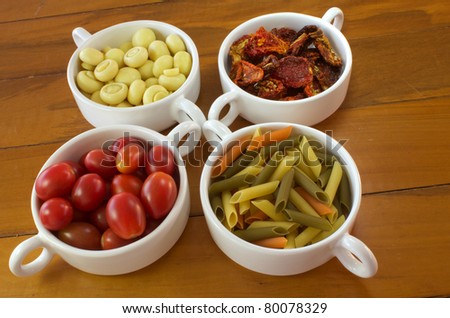 Ingredients to make a italian food, including pasta, garlic, dry tomato, basil and rosemary.