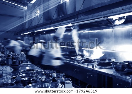 Chef in restaurant kitchen at stove with pan doing flambe on food Chef in restaurant kitchen at stove with pan doing flambe on food