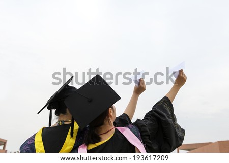 Beautiful female graduates wearing graduation gown, throwing airplane