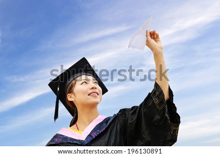 Beautiful female graduate wearing graduation gown, throwing airplane