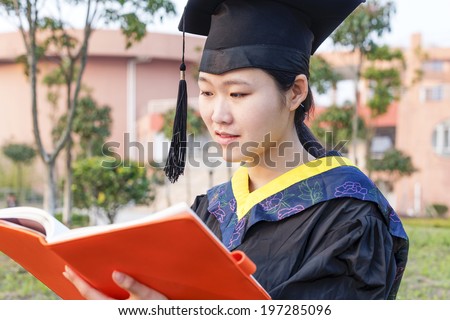 Beautiful female graduate wearing graduation gown,looking book
