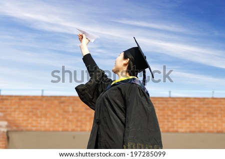 Beautiful female graduate wearing graduation gown, throwing airplane