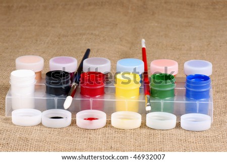 artist brushes with paint jar covers and rows of paint jars