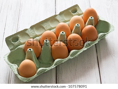 Eggs in egg-box on white wood background Nine fresh chicken eggs in green egg-box on white painted wooden background.