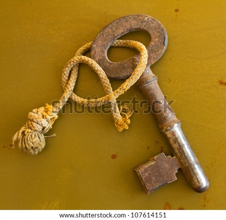 Ancient key on grunge metal background Old rusty key tied with frayed string isolated on grungy metal background.