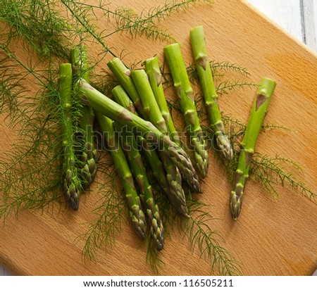Asparagus spears (Asparagus officinalis) and fern. Freshly cut green asparagus spears and fern scattered on a wooden chopping board