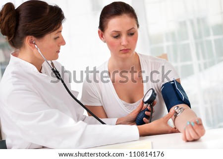 Female doctor checking young woman blood pressure