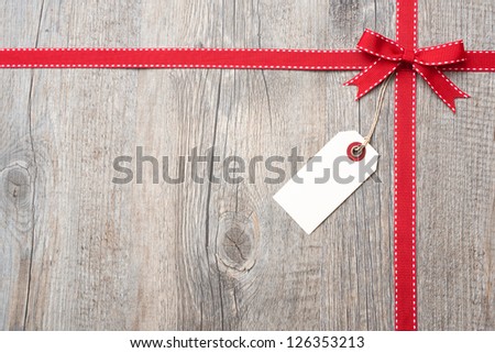Red ribbon and bow with address label attached over wooden background