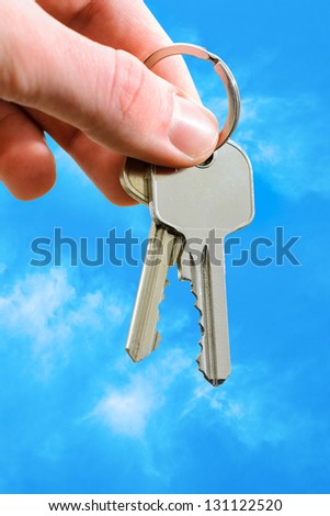 Man\'s hand holding house keys on blue sky background
