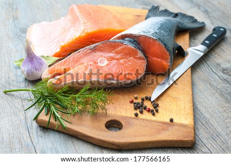 Raw salmon fish steaks with fresh herbs on cutting board Raw salmon fish steaks with fresh herbs on cutting board