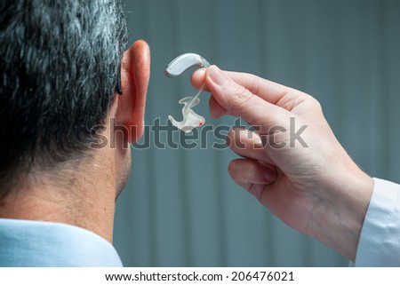 Doctor inserting hearing aid in senior\'s ear