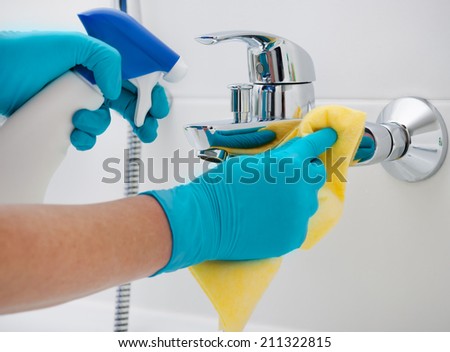 woman doing chores in bathroom, cleaning faucet with spray detergent