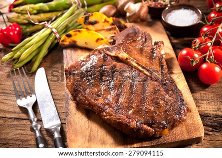 Beef steaks with grilled vegetables and seasoning on wooden background