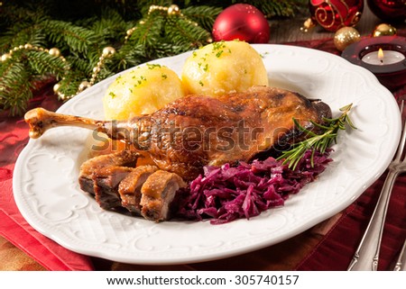 Crusty goose leg with braised red cabbage and dumplings on Christmas decorated table