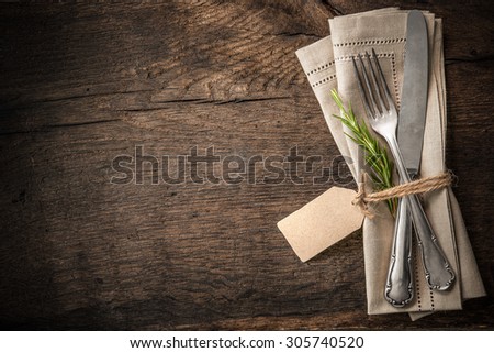 Vintage silverware with a twig of rosemary and empty tag on rustic wooden background