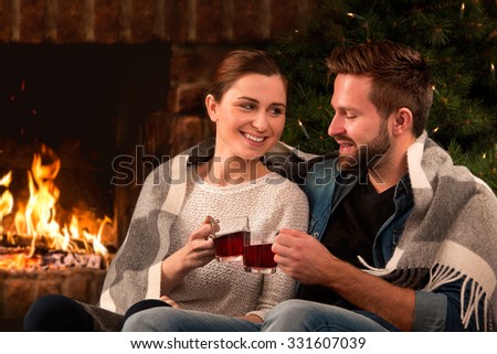 Couple relaxing with glass of wine at romantic fireplace on winter evening