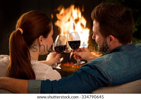 Couple relaxing with glass of wine at romantic fireplace on winter evening