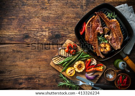 Roasted lamb meat with vegetables on grill pan on wooden background