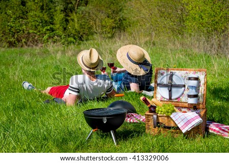 Picnic setting with red wine glasses, picnic hamper basket and burning fire in a portable barbecue