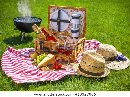 Picnic setting with red wine glasses, picnic hamper basket and burning fire in a portable barbecue