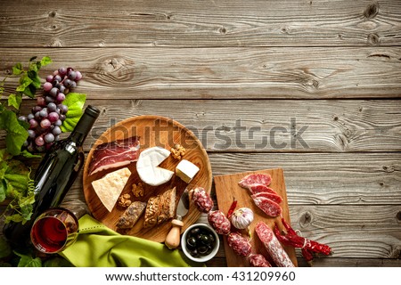 Wine bottles with grapes, cheese and traditional sausages on wooden background with copy space
