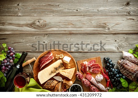 Wine bottles with grapes, cheese and traditional sausages on wooden background with copy space