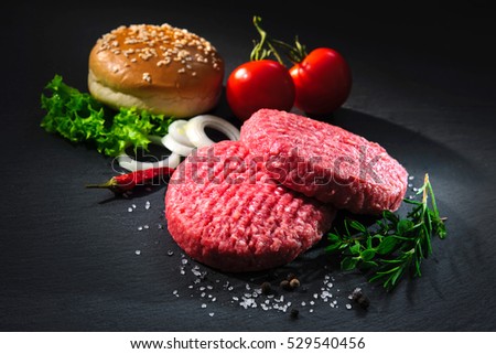 Homemade hamburger. Raw beef patties, sesame buns with other ingredients for hamburgers on dark slate plate
