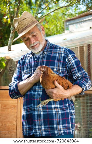 Happy organic farmer holds chicken in his arms in front of hen house