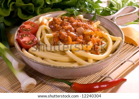 Freshly cooked plate of macaroni bolognese topped with tomato and basil