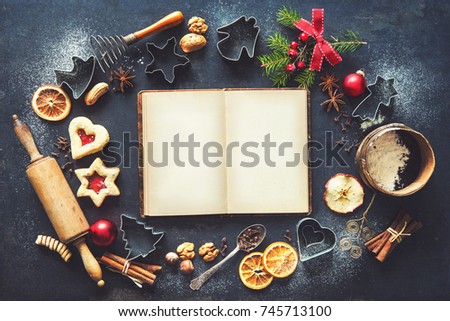 Christmas baking sweet food frame with recipes book, homemade cookies, spices, kitchen utensils, fir branches and red holiday decoration on dark rustic baking tray. Top view