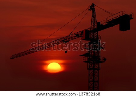 Industrial construction cranes and building silhouettes over sun at sunrise.