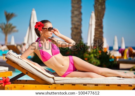 Woman sunbathing in bikini at tropical travel resort. Beautiful young woman lying on sun lounger near pool