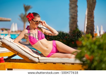 Woman sunbathing in bikini at tropical travel resort. Beautiful young woman lying on sun lounger near pool