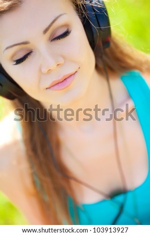 Close portrait of young beautiful smiling woman in headphones outdoors in summer